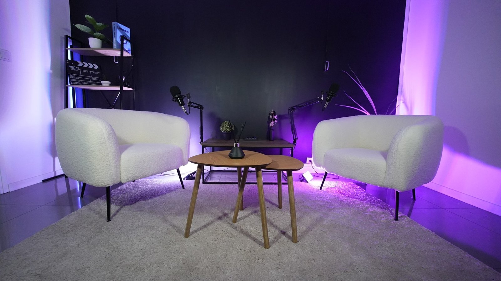 Les deux fauteuils blancs et les micros du studio, sous une lumière violette
